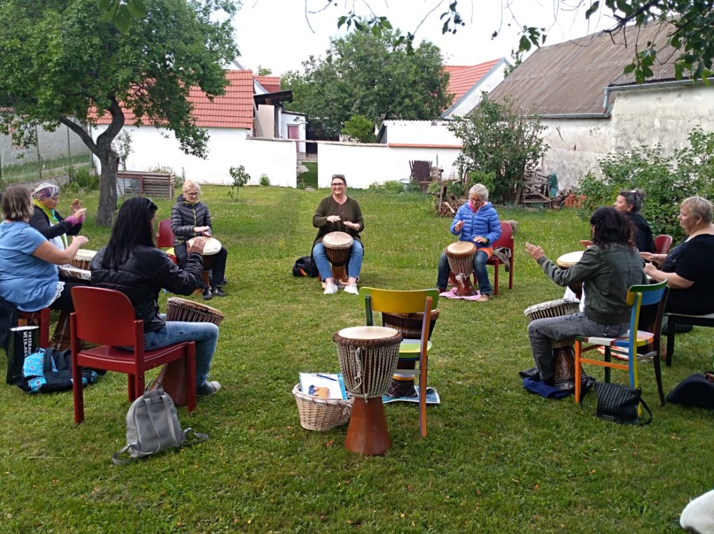 Menschen sitzen mit ihren Trommeln im Garten im Kreis