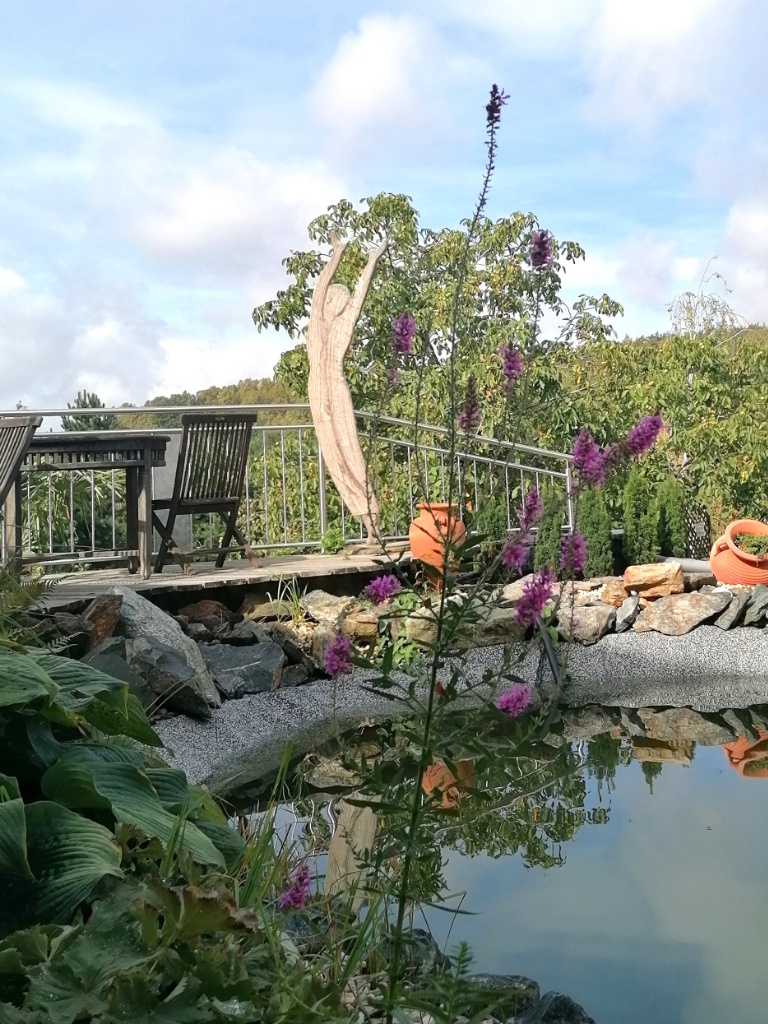 Blick vom Teich zur Holzstatue