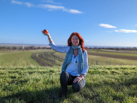 Karin in der Hocke mit einem Apfel in der rechten Hand