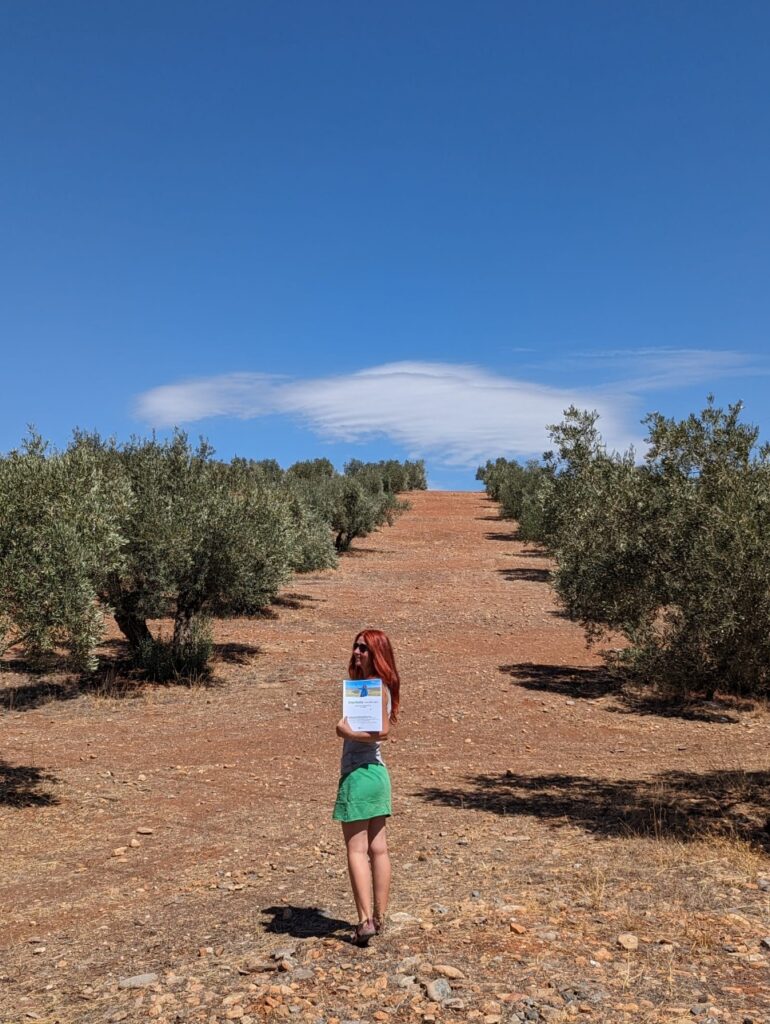 Karin zwischen Olivenbäumen, mit ihrer Starthilfe in der Hand