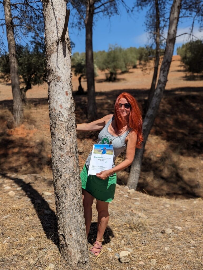 Karin schaut hinter einem Baum hervor, mit dem Freebie in der Hand