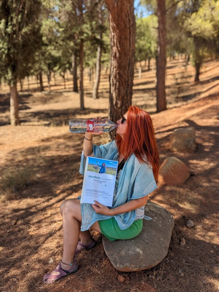 Karin sitzt auf einem Stein und trinkt Wasser aus einer Flasche