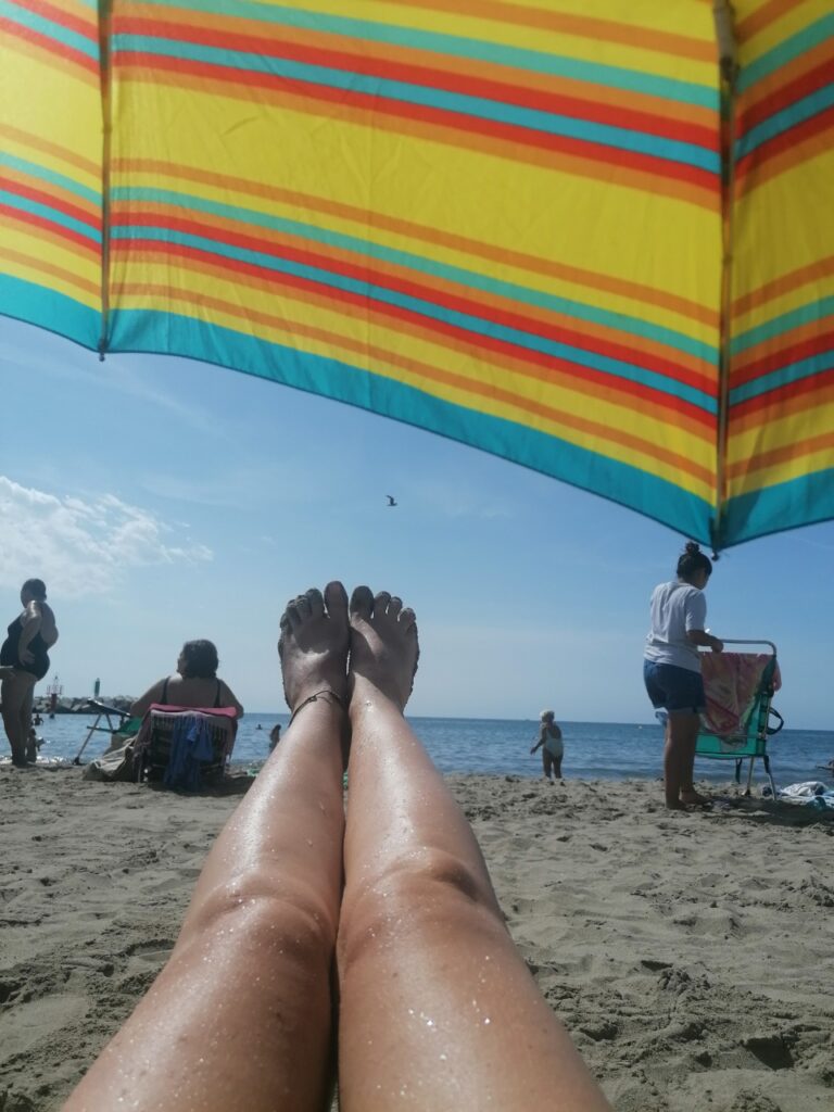 Karins Beine unterm Sonnenschirm - Richtung Meer fotografiert