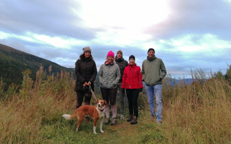 5 Personen und 1 Hund auf einer Wiese, im Hintergrund Berge