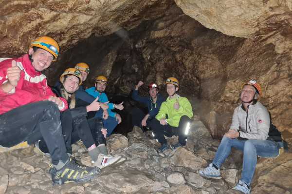 Menschen sitzen in einer dunklen Höhle mit gelben Helmen und lachenden Gesichtern
