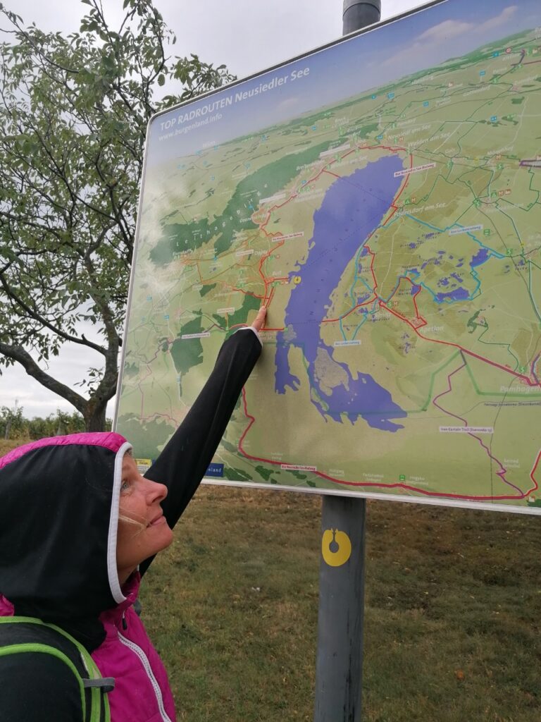 Babsi zeigt auf auf einem Schild mit dem Neusiedlersee, wo wir uns gerade befinden.