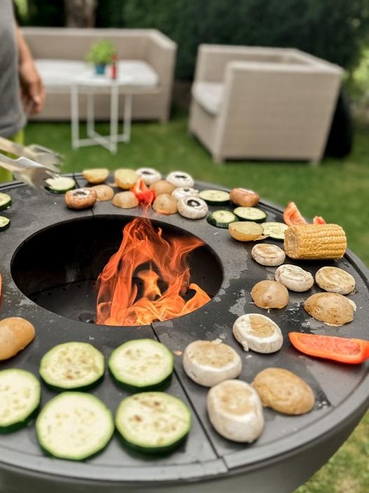 Feuerstelle mit Grill, auf dem viel Gemüse liegt