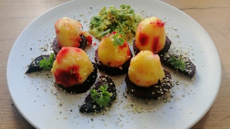 Gedämpftes Gemüse mit Avocadocreme auf einem Teller. 6 halbe Karoffeln thronen auf 5 Rote-Rüben-Scheiben.
