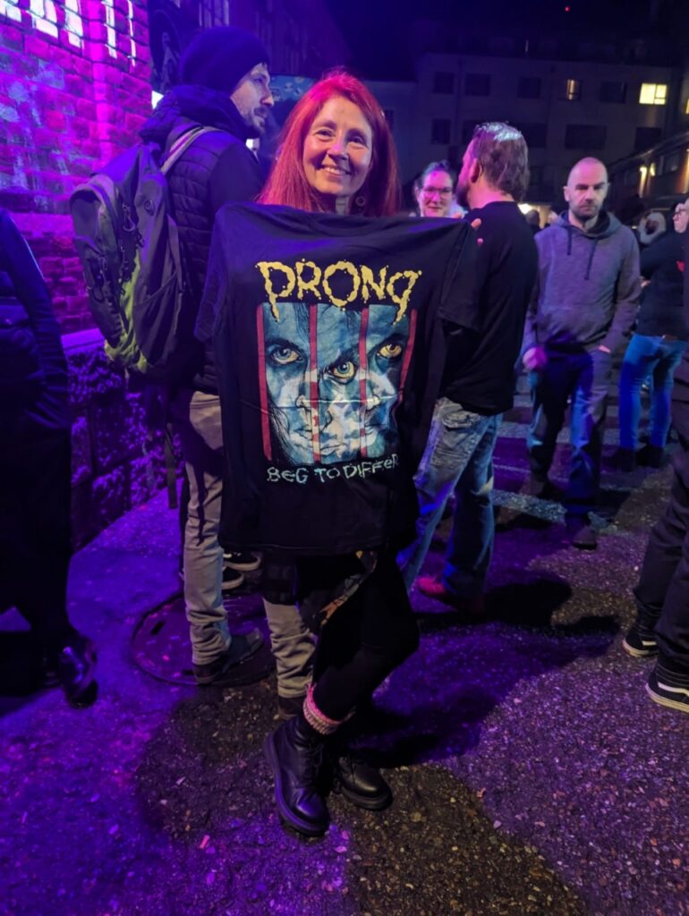 Karin vor der Konzerthalle mit Prong T-Shirt,, das sie vor sich hinhält