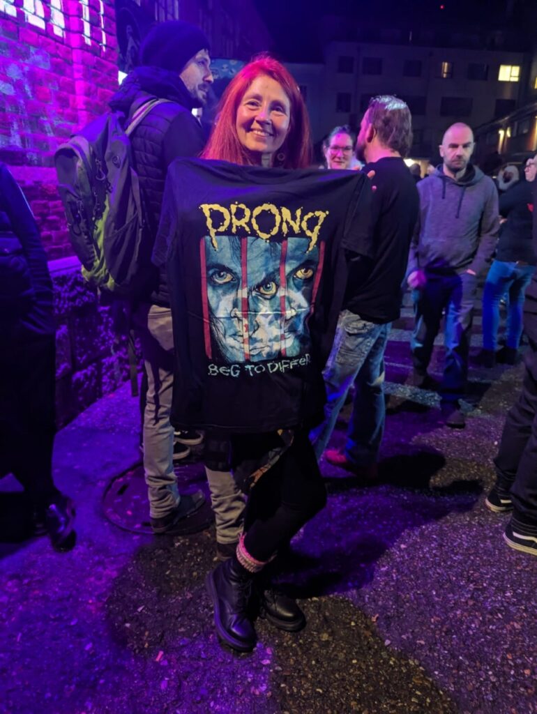 Karin vor der Konzerthalle mit Prong T-Shirt,, das sie vor sich hinhÀlt