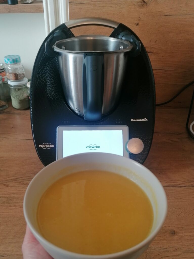Suppenschüssel mit gelber Suppe, im Hintergrund ein schwarzer Thermomix