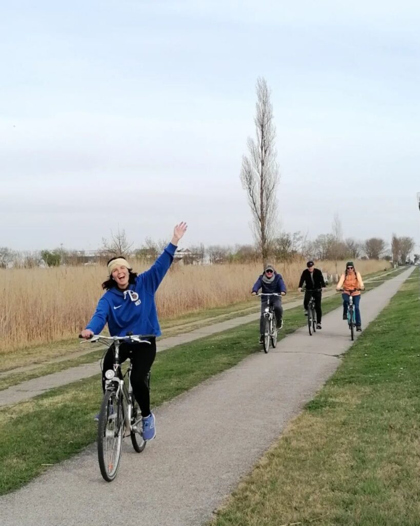 4 Personen auf dem Fahrrad. Das junge Mädl fährt winkend an der Spitze.