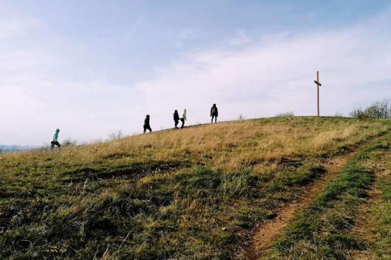 Menschen bewegen sich in weiter Ferne auf ein Kreuz zu, das auf einem Hügel steht