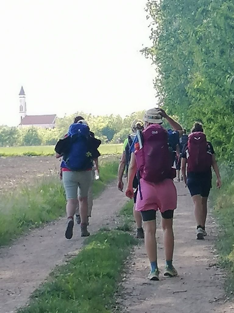 Wandergruppe von hinten, in der Ferne die Kirche