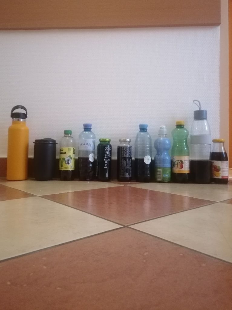 11 Flaschen, gefüllt mit Saft stehen aufgereiht auf dem Fliesenboden