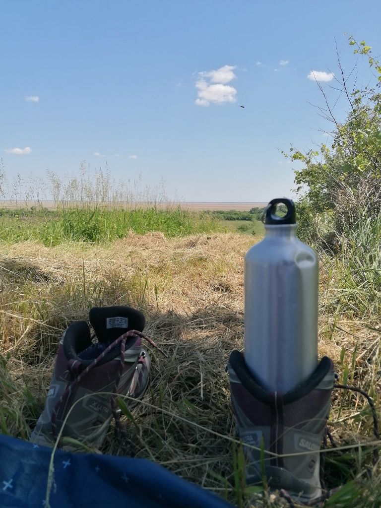 Wasserflasche im Wanderschuh, dahinter Landschafts-Ausblick
