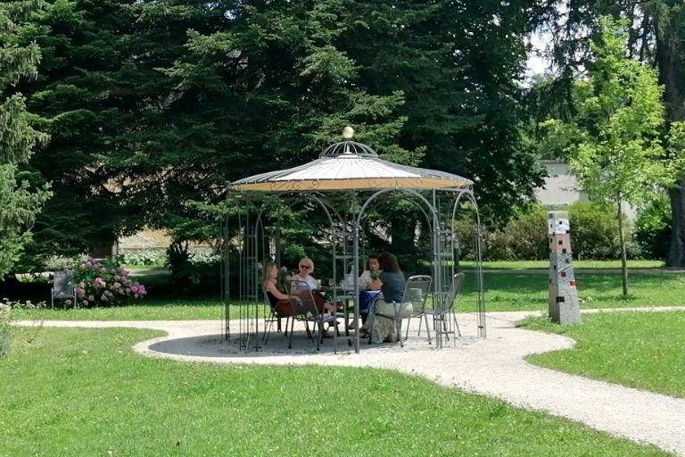Ein Weg führt zu einem Pavillon. Rundherum Wiese und im Hintergrund hohe Bäume.
