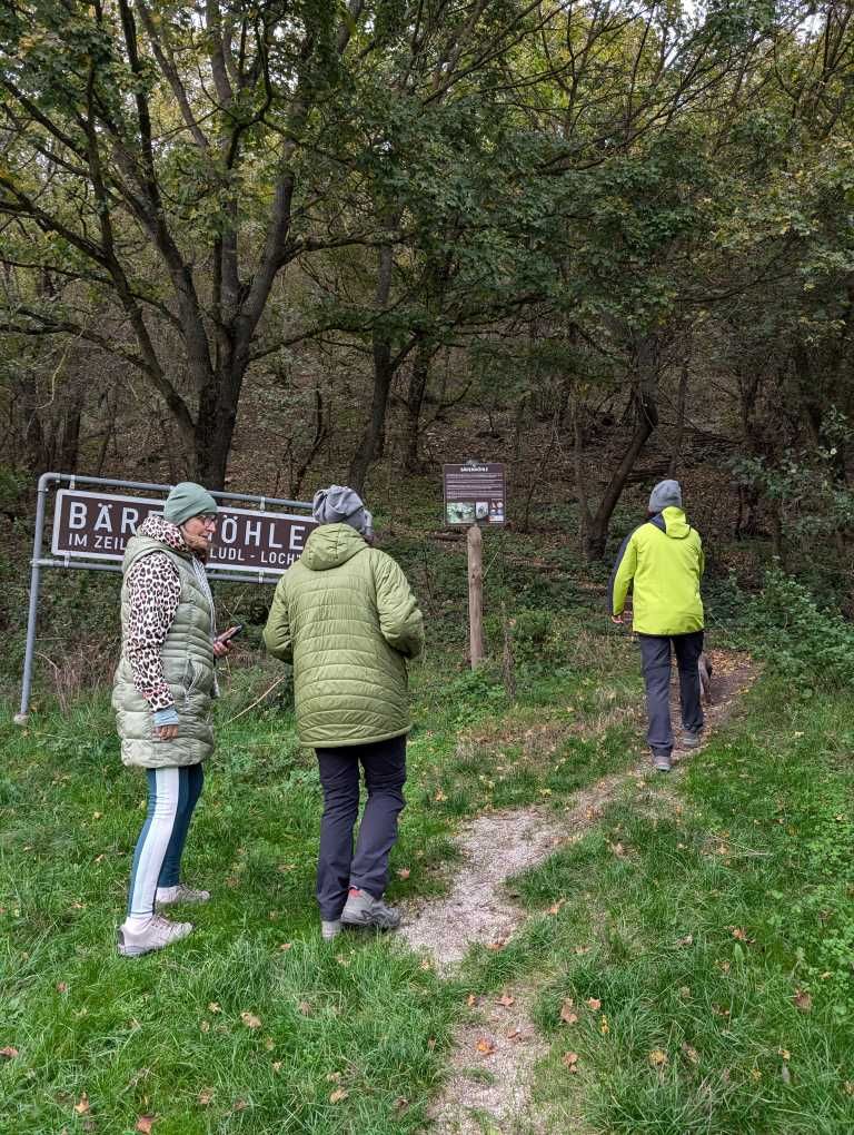 Die drei Teilnehmerinnen vor dem Schild "Bärenhöhle" , daneben der Waldweg, der zur Höhle am Zeilerberg führt