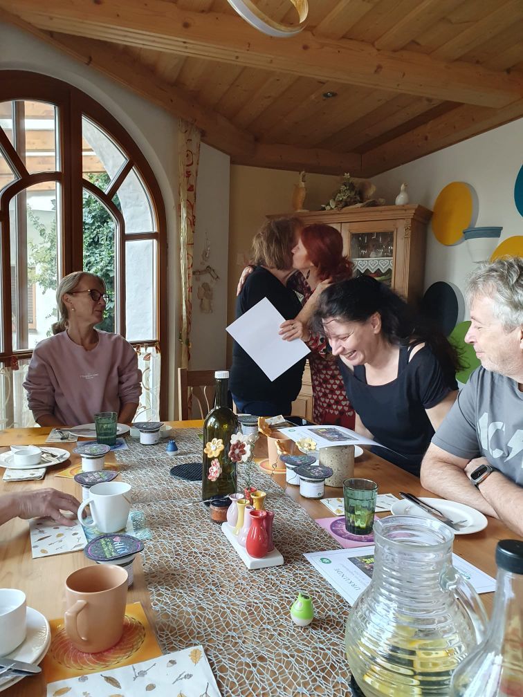 Gruppe am Frühstückstisch, im Hintergrund Umarmung