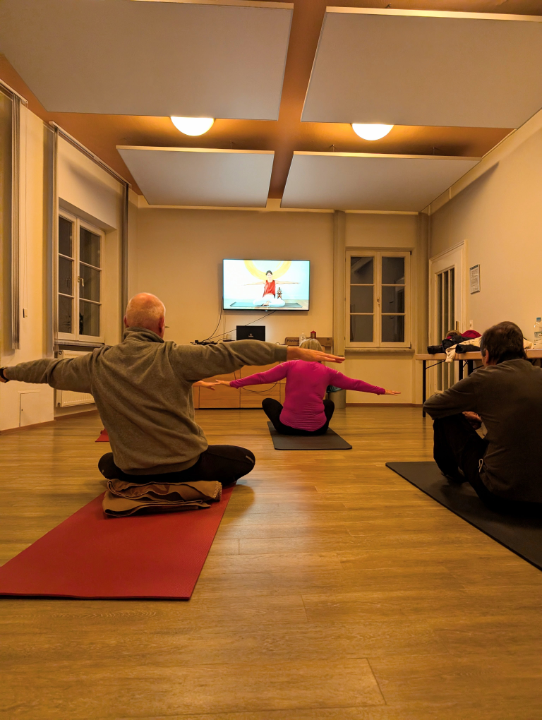 3 Teilnehmer sitzend auf der Yogamatte mit zur Seite gestreckten Händen