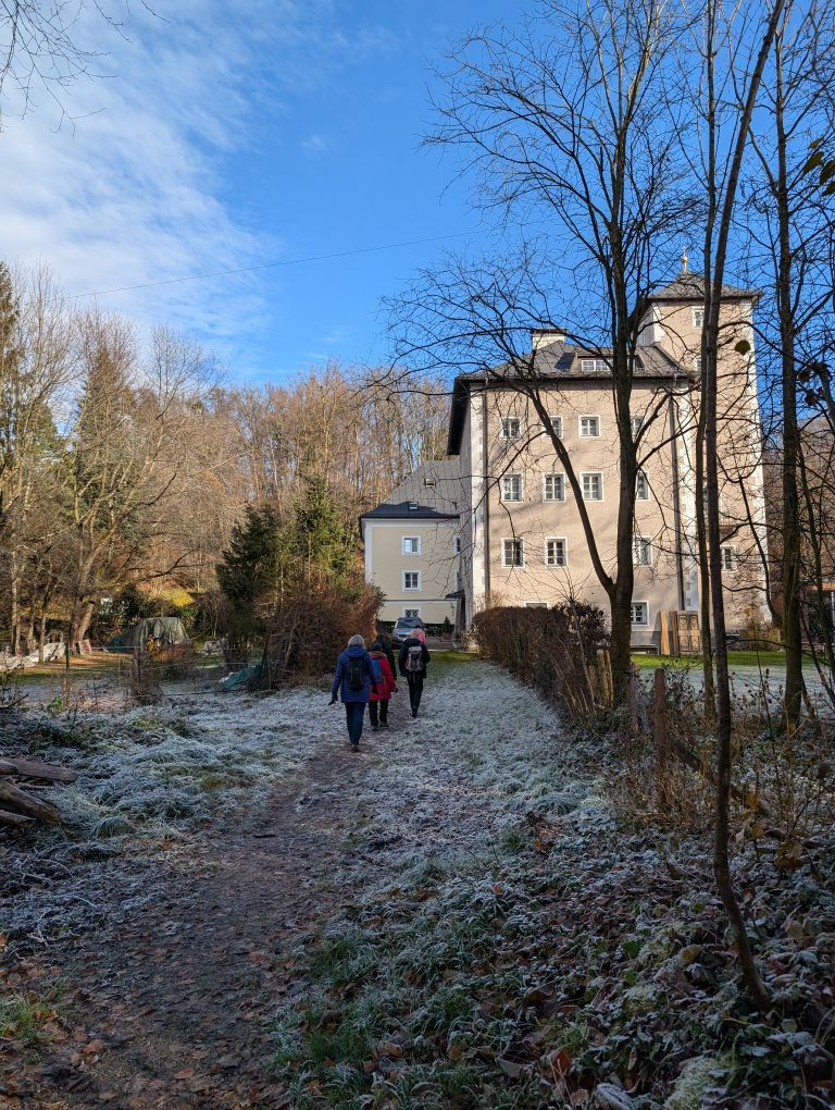 Gruppe von hinten in bewaldeter, weiß-gefrorener Umgebung. Rechts steht ein großes Haus.
