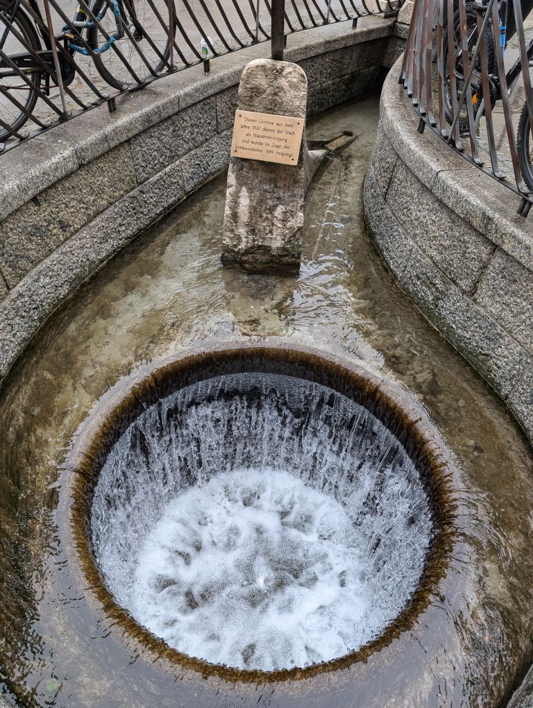 Blick auf eine offene runde Stelle im Boden, das den Blick auf rinnendes Wasser freigibt