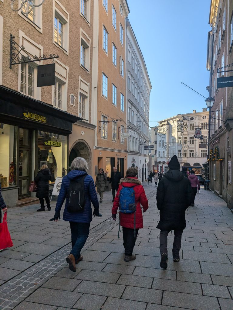 Fastengruppe von hinten, durch eine Einkaufsstraße zwischen hohen Häusern bummelnd