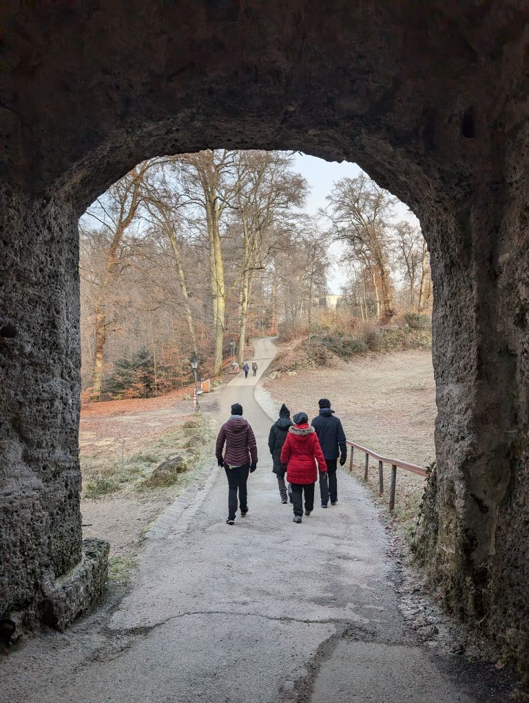 Blick durch ein Tor auf einen Weg mit gehenden Menschen von hinten
