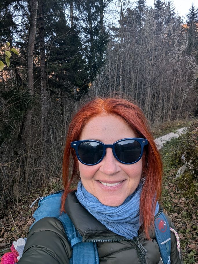 Selfie: Karin mit Sonnenbrille, im Hintergrund ein schmaler Waldweg, rundherum Bäume