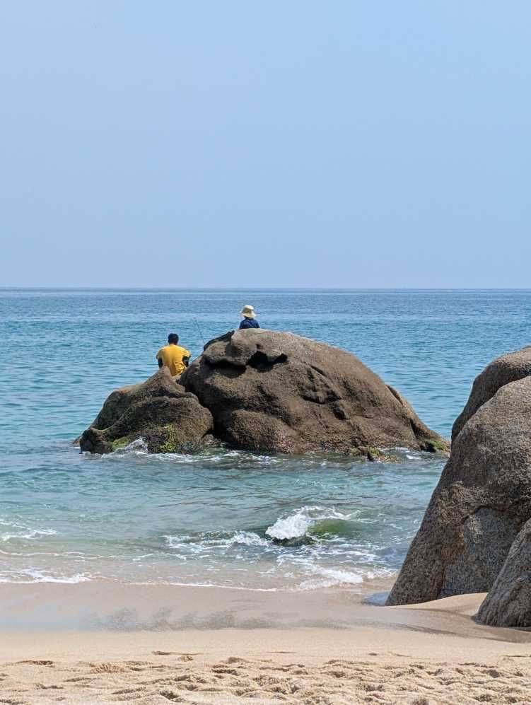 2 Fischer sitzen auf einem Felsen im Meer