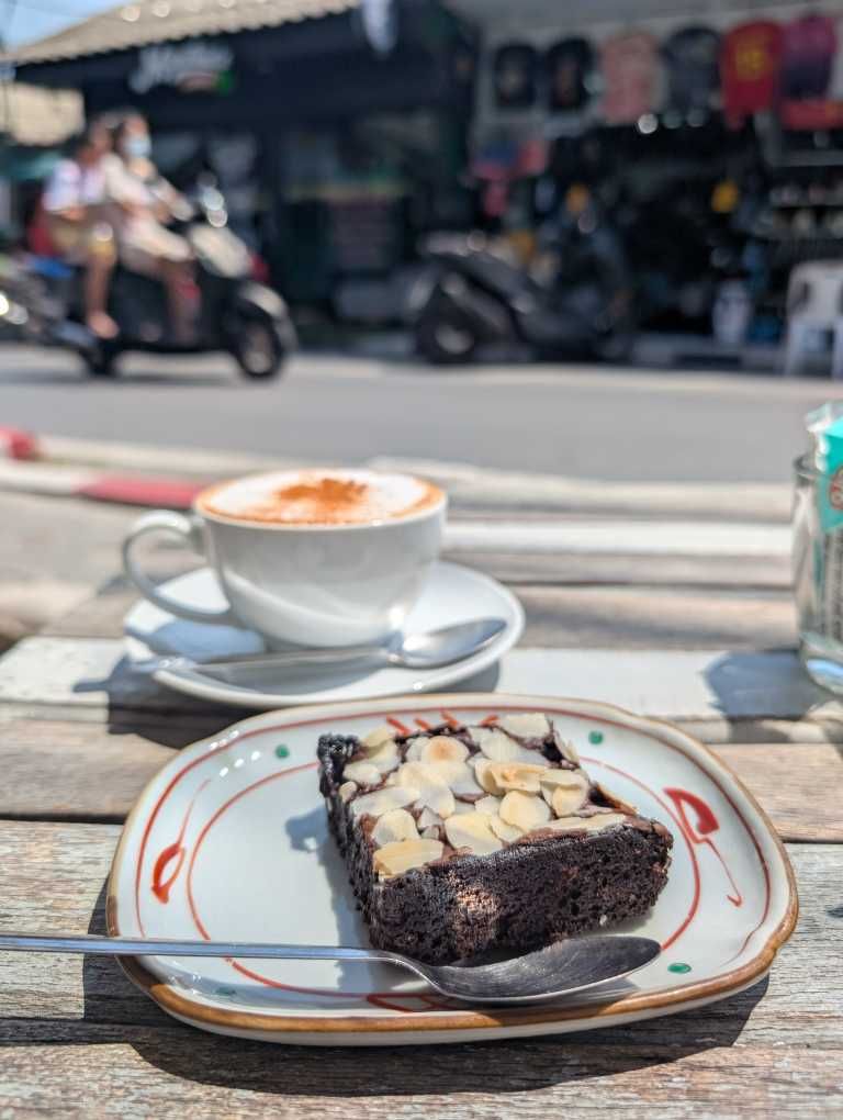 Teller mit kleinen, dunklen Schokokuchen und einer Tasse Kaffee im Hintergrund.