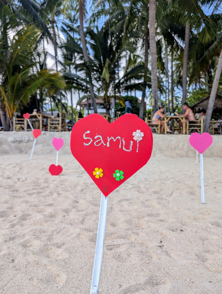 Rotes Holzherz mit Aufschrift "Samui", steckt im Sand