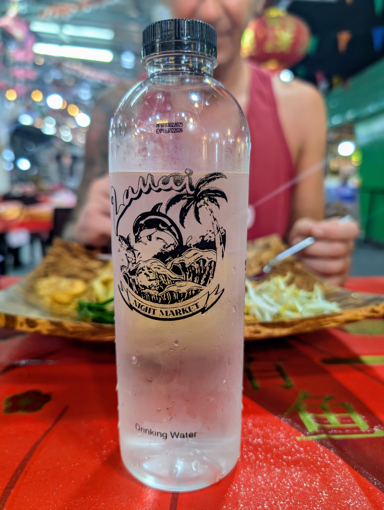 Wasserflasche, im Hintergrund ein Pad Thai Gericht