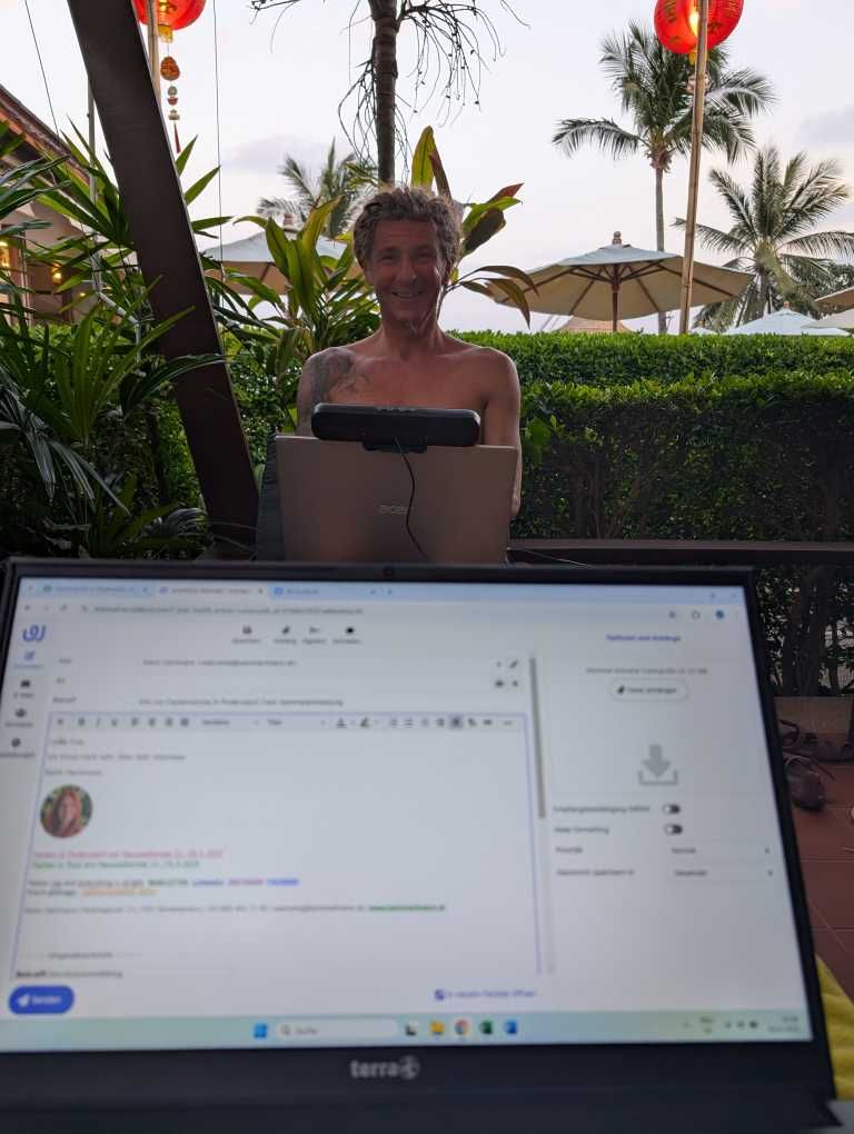Aufgeschlagener Laptop, Blick nach draußen zu Palmen und Pool