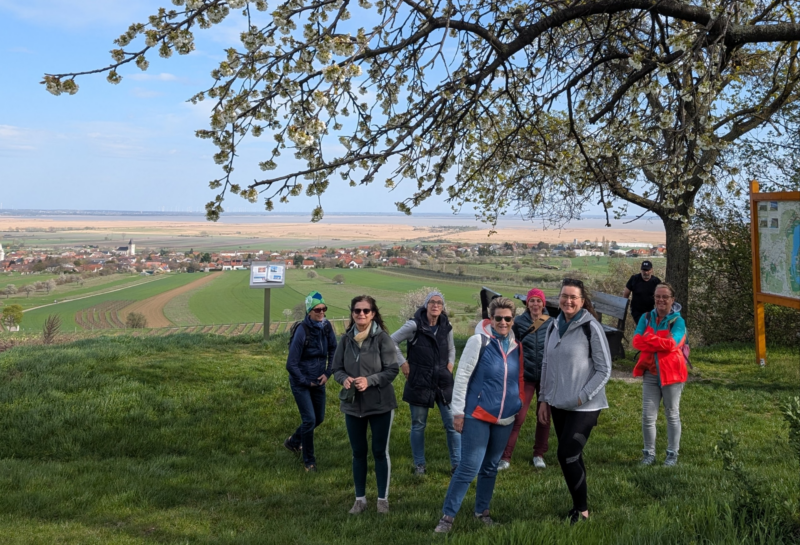 Teilnehmer stehen unter einem blühenden Kirschenbaum, im Hintergrund Weingärten, Schilfgürtel und Neusiedlersee