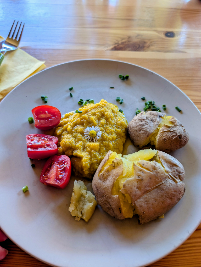 Teller mit zwei Kartoffeln,  Gemüsepürree und 3 halben Cocktail-Tomaten, garniert mit einem Gänseblümchen und Schnittlauch