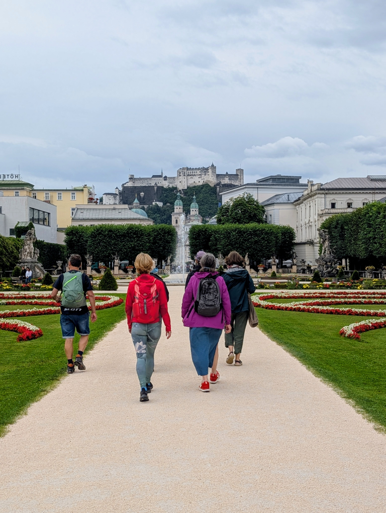Fastengruppe von hinten, spazierend durch den Mirabellgarten, im Hintergrund ein Springbrunnen, an den Seiten Wiese und Blumen