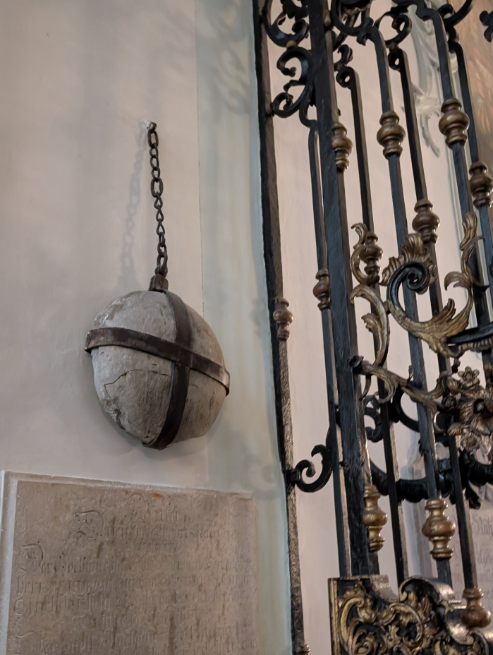Runder Stein hängt mit Eisenkette an der Kirchenwand