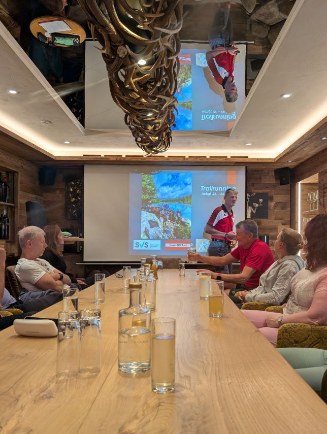 Tisch mit Teilnehmern, am Tischende Leinwand