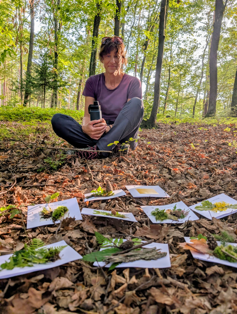 Ute sitzt am Waldboden, vor ihr liegen die kreativen Kunstwerke