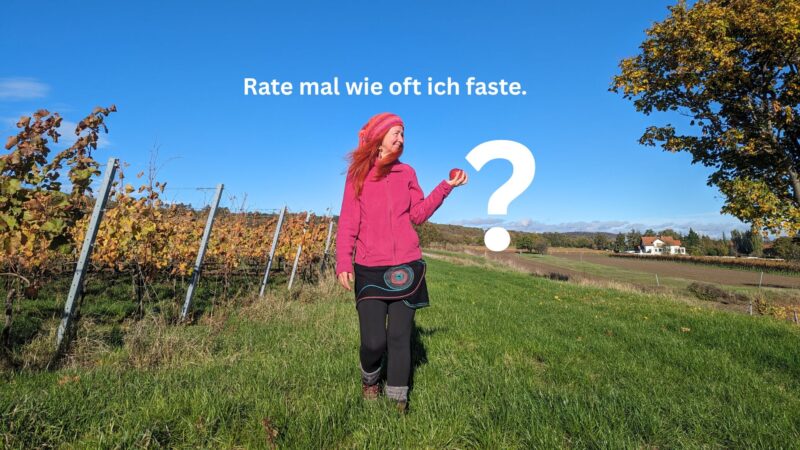 Karin geht auf einer Wiese auf dich zu. Links von ihr sind Weingärten, rechts ein Baum. In ihrer rechten Hand trägt sie einen roten Apfel. Auf dem Bild steht drauf: "Rate mal wie oft ich faste."?