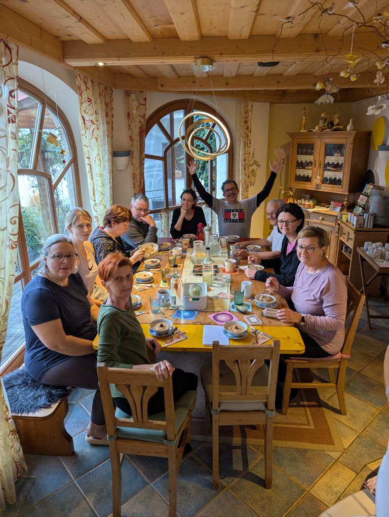 Gemütliches Esszimmer. Am Tisch sitzen 10 Fastende. Jener am Tischende sitzt begeistert mit erhobenen Händen.