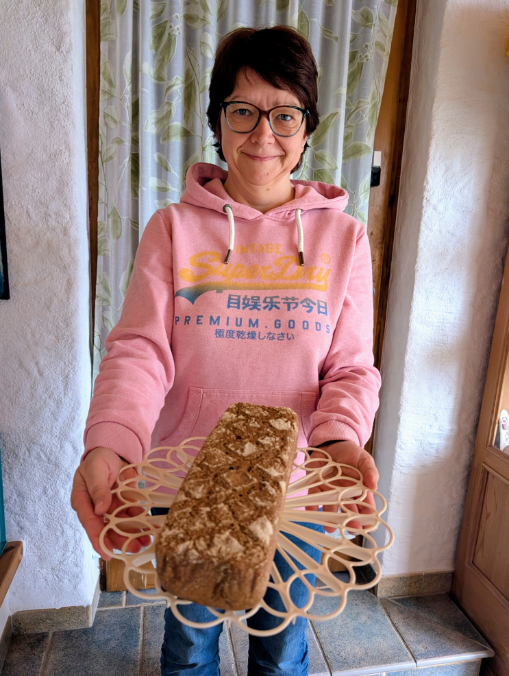 Frau hält einen länglichen, eckigen Brotlaib in die Kamera