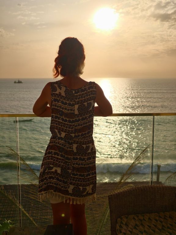 Karin von hinten am Balkon, mit Blick auf das Meer bei Sonnenuntergang 