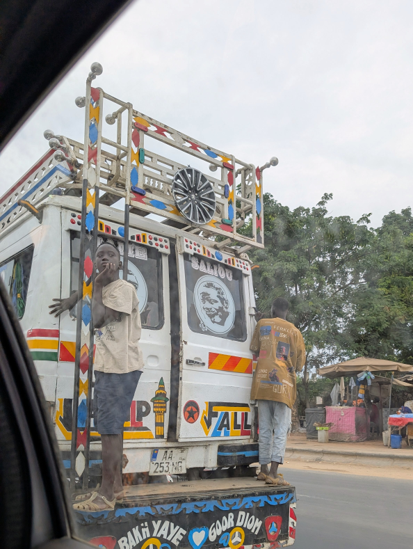 Bunter Bus auf der Straße. Hinten stehen zwei Menschen drauf
