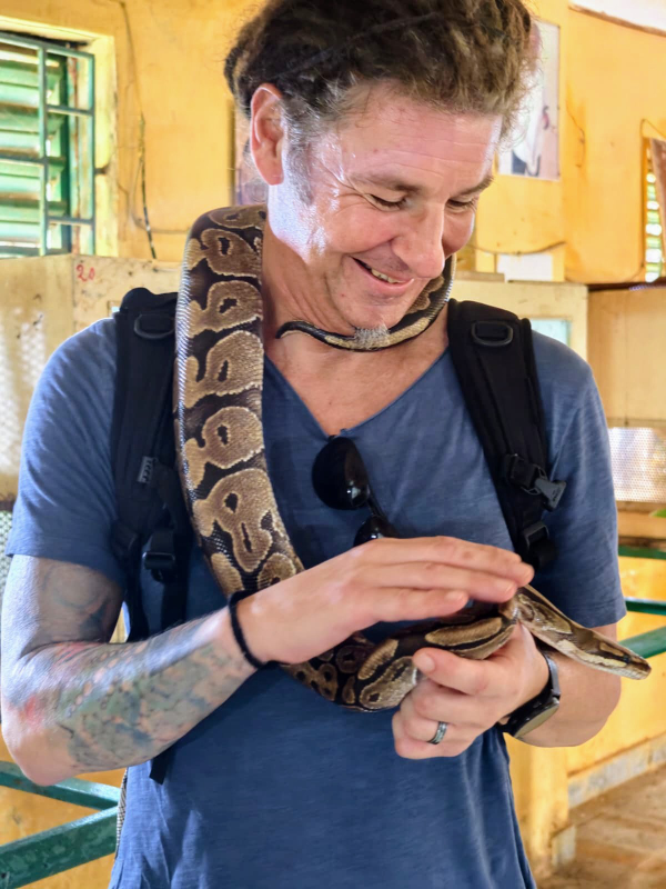 Seppi hat eine Schlange umgehängt, die er streichelt.