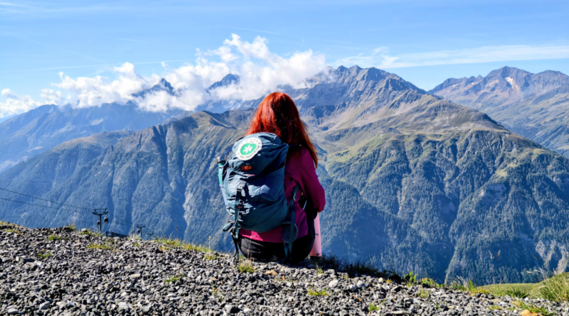 Karin am Abgrund sitzend von hinten mit Blick auf die Berge