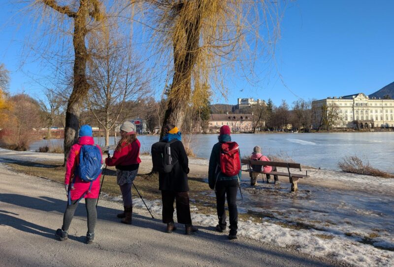 Fünf Menschen von hinten in bunter Winterkleidung vor dem zugefrorenen Teich.