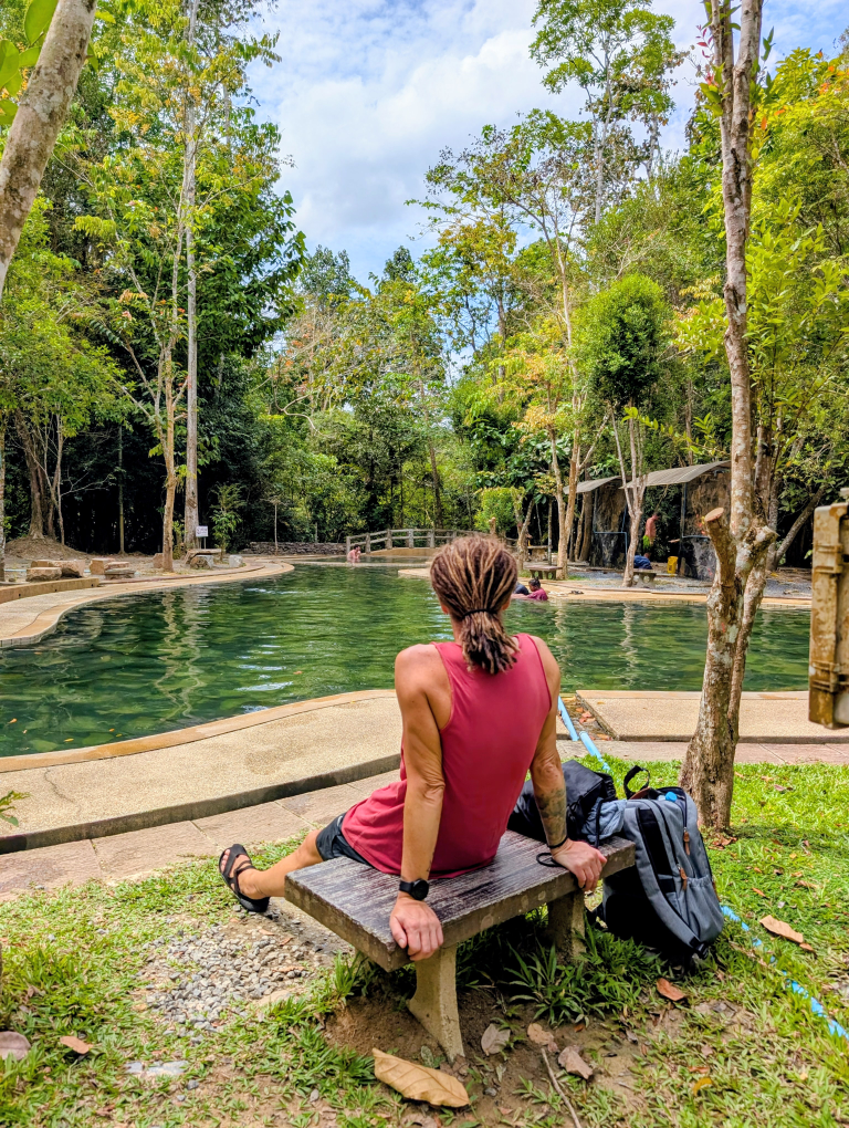 Seppi von hinten, sitzend auf einer Bank, mit Blick auf den heißen Pool