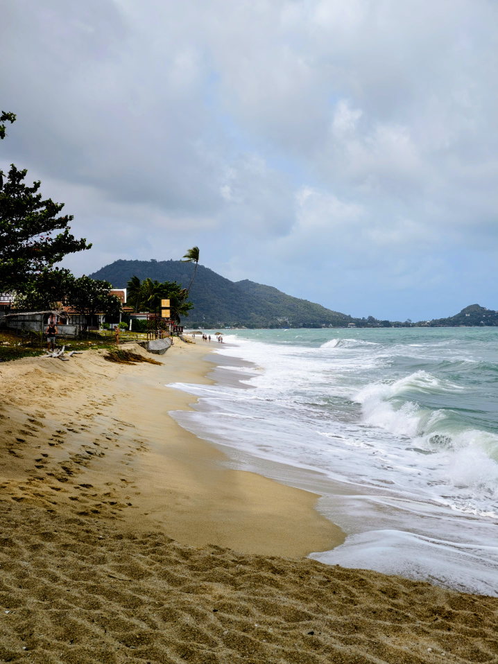 Links abfallender Sandstrand, rechts Meer, In der Ferne ein bewaldeter Berg